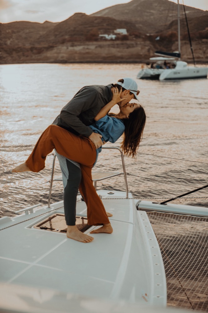 Paar küsst sich auf dem Boot bei Sonnenuntergang – Caldera Santorini, SAPHIR WEDDINGS