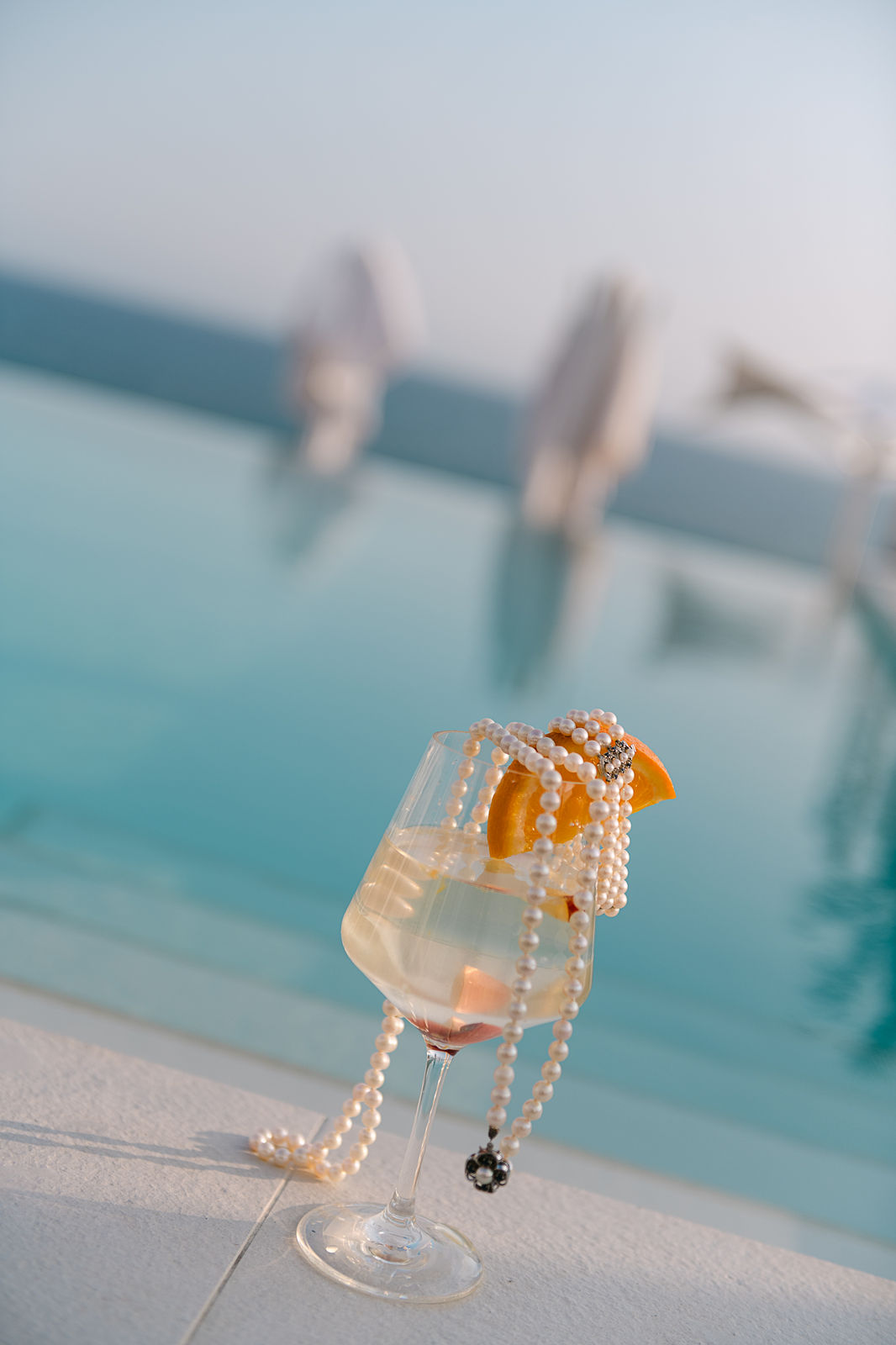Pearl necklace and cocktail at Santorini infinity pool – luxury destination wedding photography Saphir Weddings
